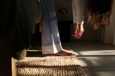 Eine Frau mit langen brauen Haaren steht kopfüber gebeugt und lässt die Arme an den Füßen baumeln