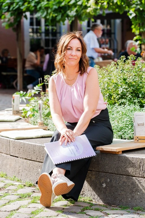 Ramona Leis - Pädagogin für Mindset-Entwicklung - Frau sitzt auf einer Steinmauer und hält ein Heft in der Hand